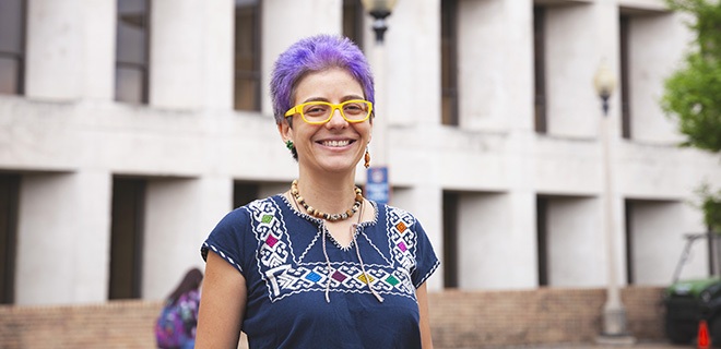 Woman in blue shirt with purple hair stands in front of white building