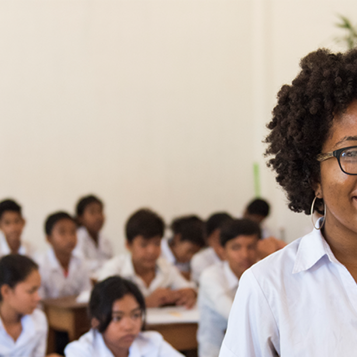 Female smiling in white shirt in classroom with students sitting at desks in the background