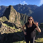 Woman on hill doing hook'em sign in front of Machu Picchu.